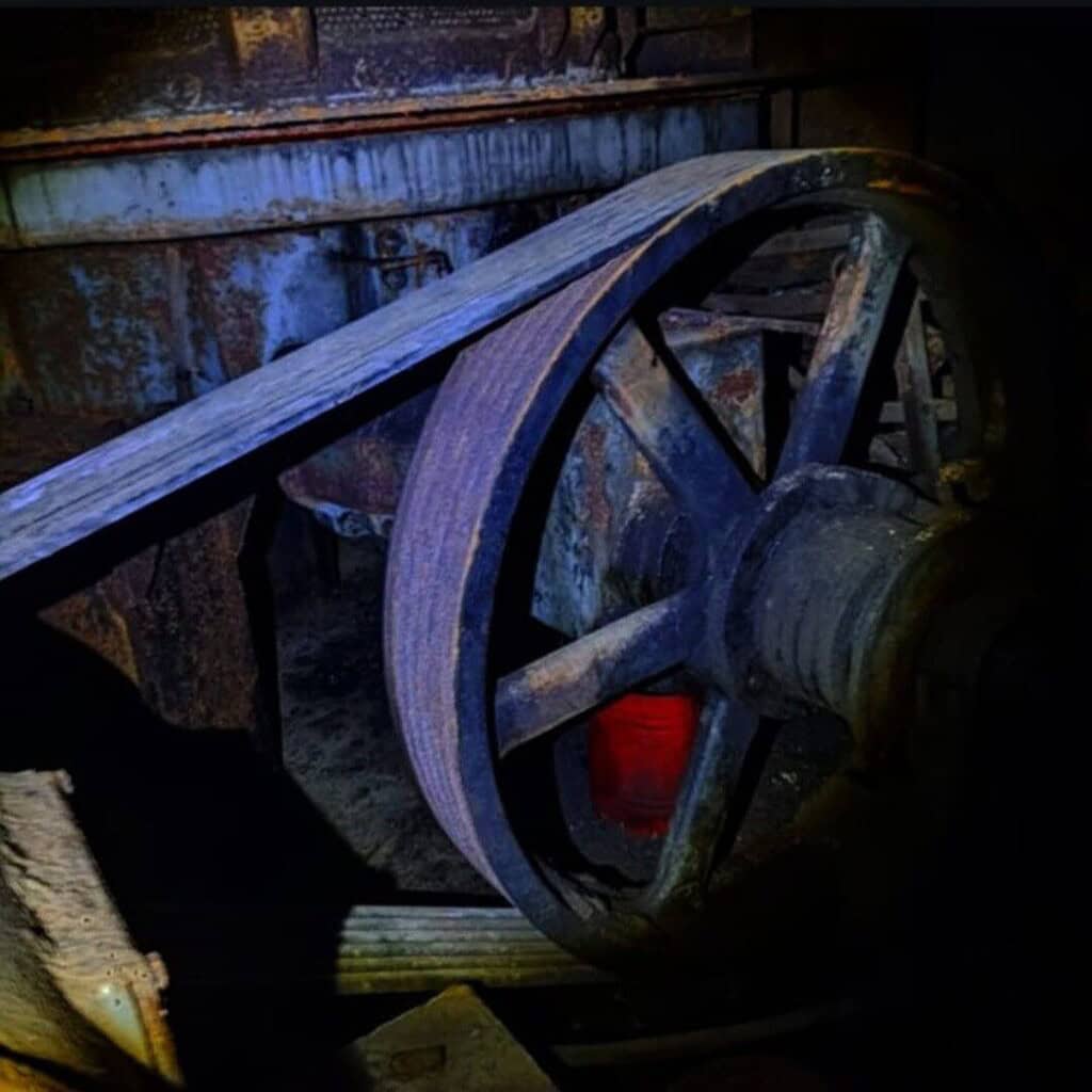 Rusty industrial pulley wheel in abandoned factory with decayed machinery and eerie lighting.