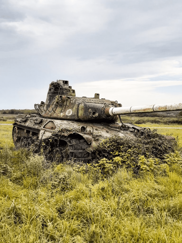 Abandoned rusted tank in overgrown field, nature reclaiming military relic, urbex exploration scene.