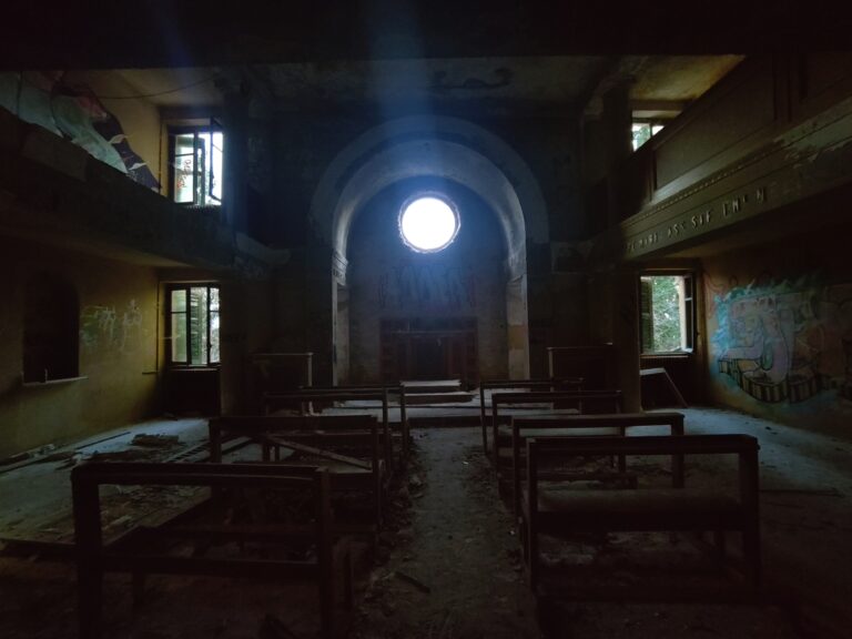 Abandoned chapel interior with decaying benches, peeling walls, dim lighting, and graffiti.
