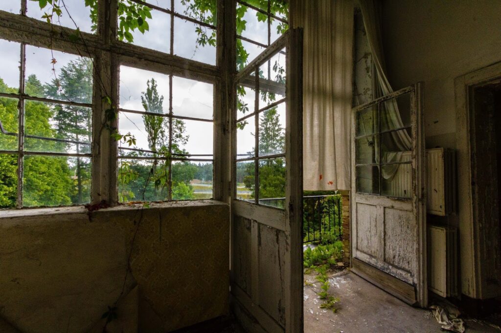 Abandoned balcony with decaying door, nature reclaiming space, urban exploration scene.