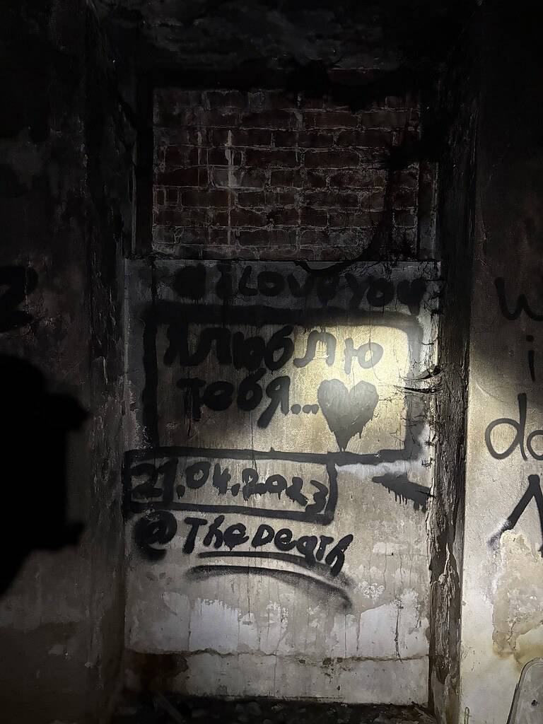 Graffiti auf einer Backsteinmauer an einem verlorenen Ort, mit einem Herz und Text, das die unheimliche Atmosphäre verlassener Orte einfängt.