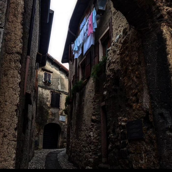 Historic European alleyway with stone buildings, hanging laundry, and cobblestone path.